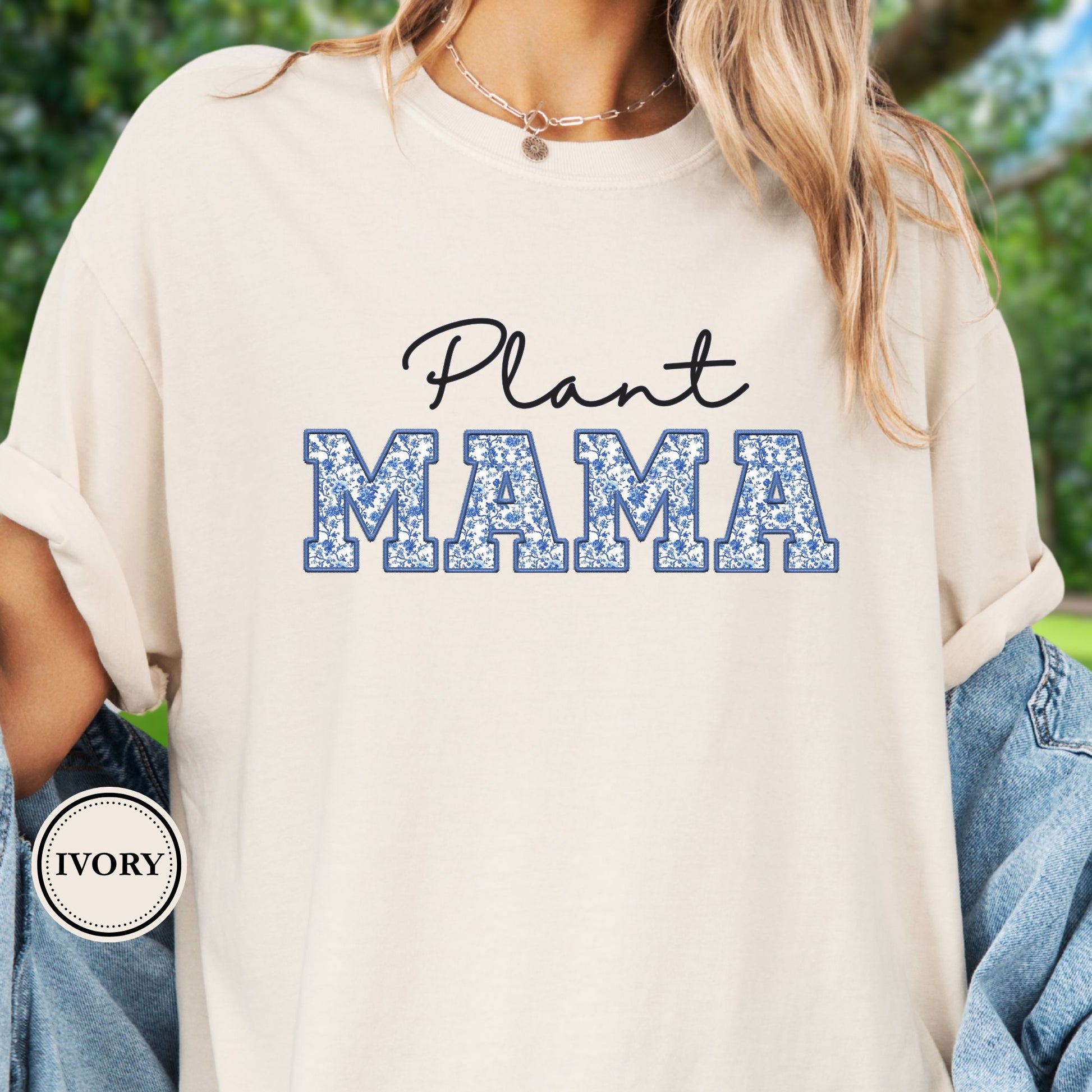Model wears an ivory  t-shirt with 'Plant Mama' text on a blurred green background
