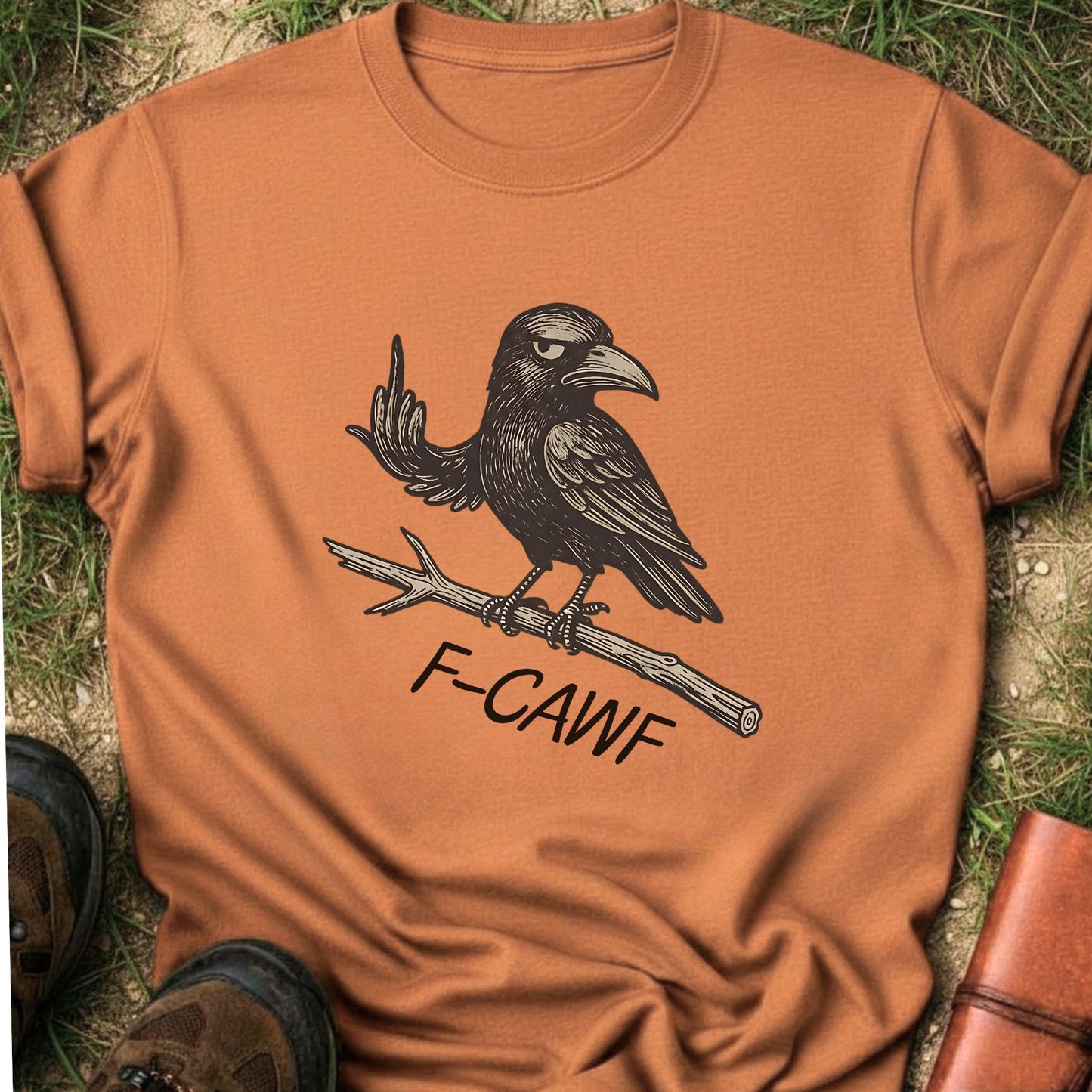 Orange  t-shirt with a crow illustration makine a rude gesture with his wing and 'F-CAWF' text on a grass surface