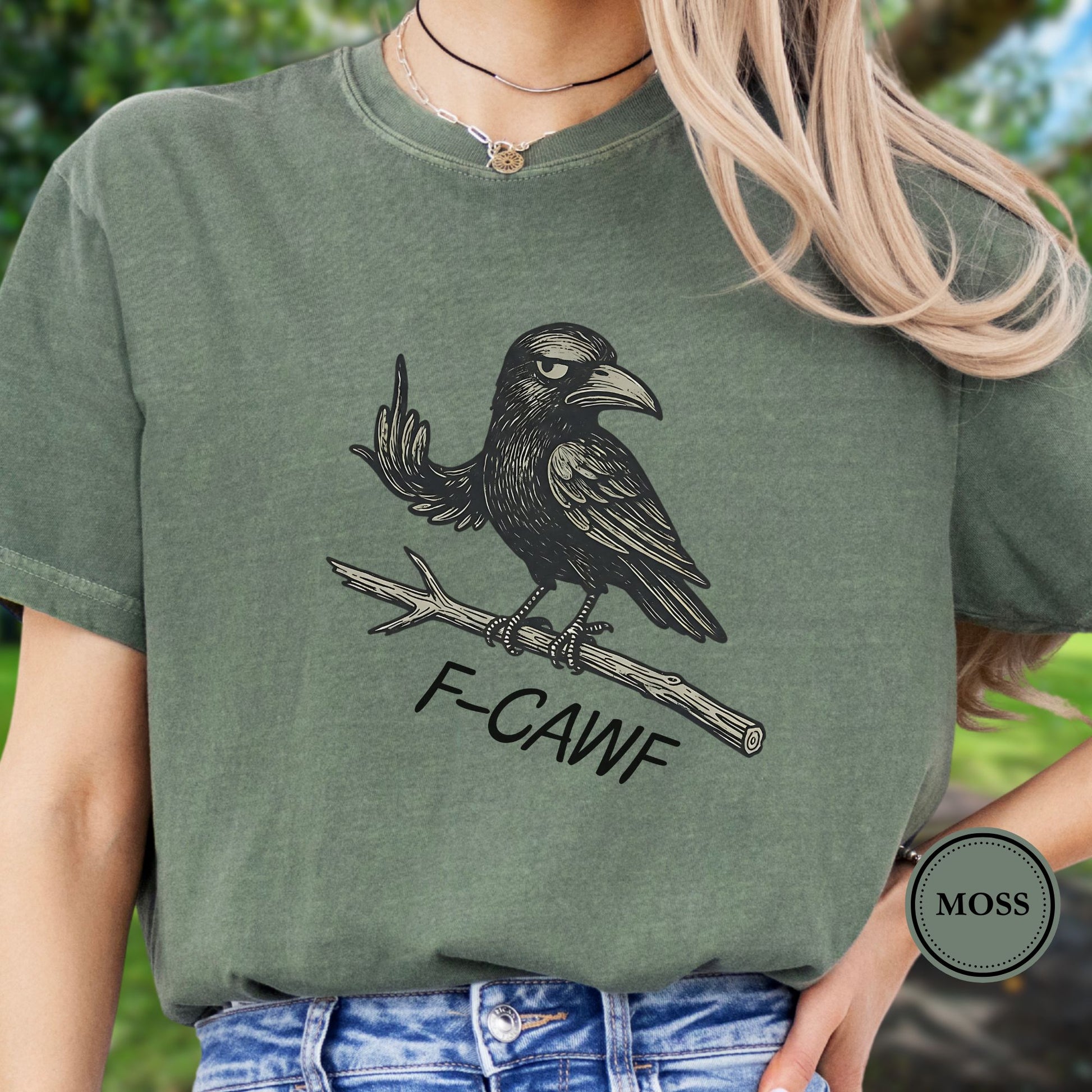 Person wearing a green  t-shirt with a crow illustration makine a rude gesture with his wing and 'F-CAWF' text with a blurred green background