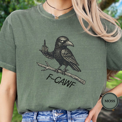 Person wearing a green  t-shirt with a crow illustration makine a rude gesture with his wing and 'F-CAWF' text with a blurred green background