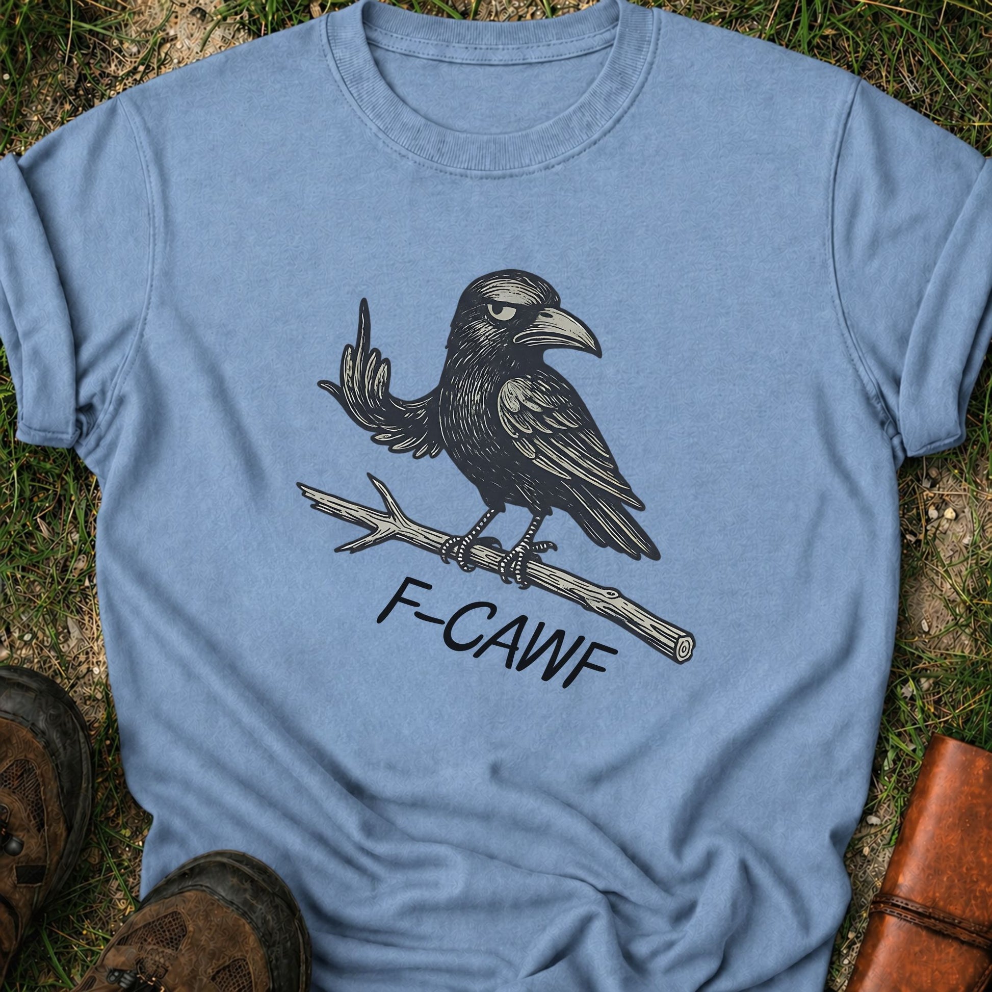 Blue  t-shirt with a crow illustration makine a rude gesture with his wing and 'F-CAWF' text on a grass surface