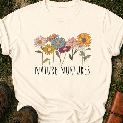 Ivory t-shirt with colorful floral design and 'Nature Nurtures' text laying  on grass.