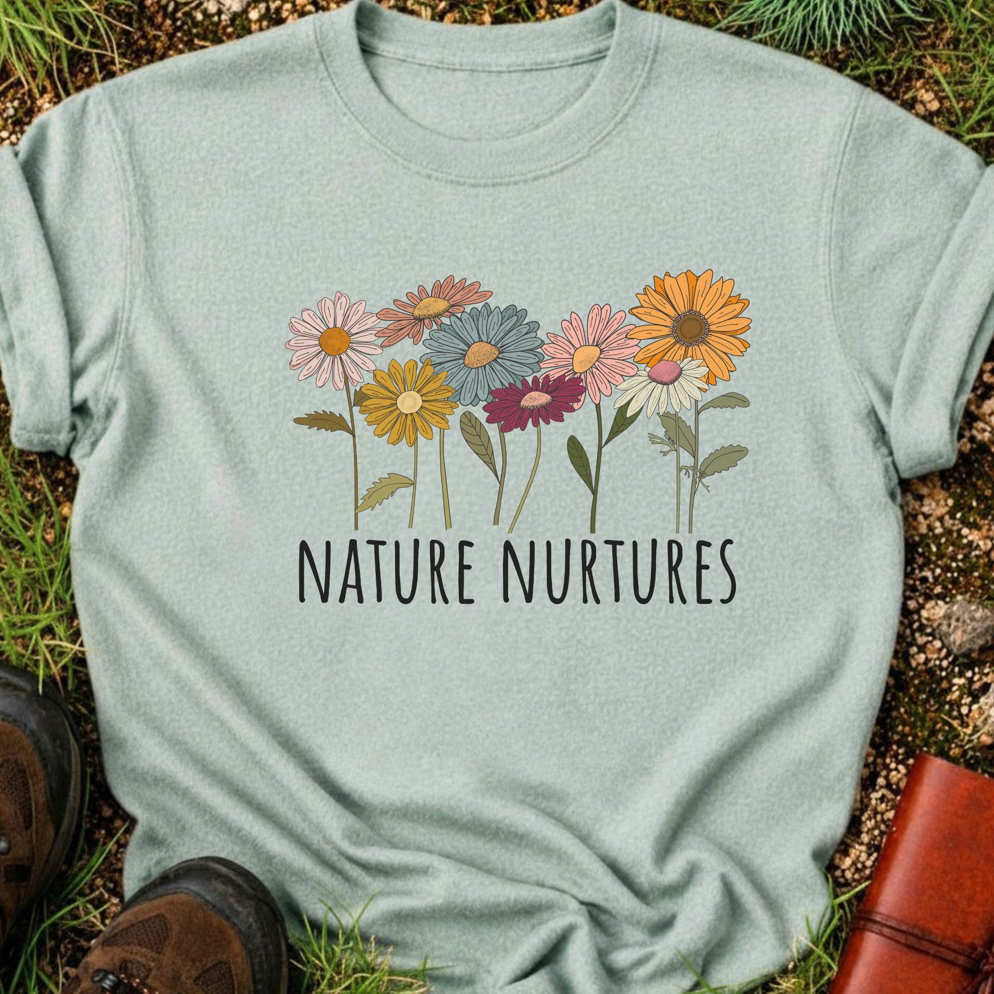 Light Green t-shirt with colorful floral design and 'Nature Nurtures' text laying  on grass.