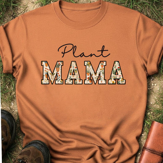 orange t-shirt with 'Plant MAMA' text filled with cheerful potted plants and florals within the letters.  The tee is lying flat on grass