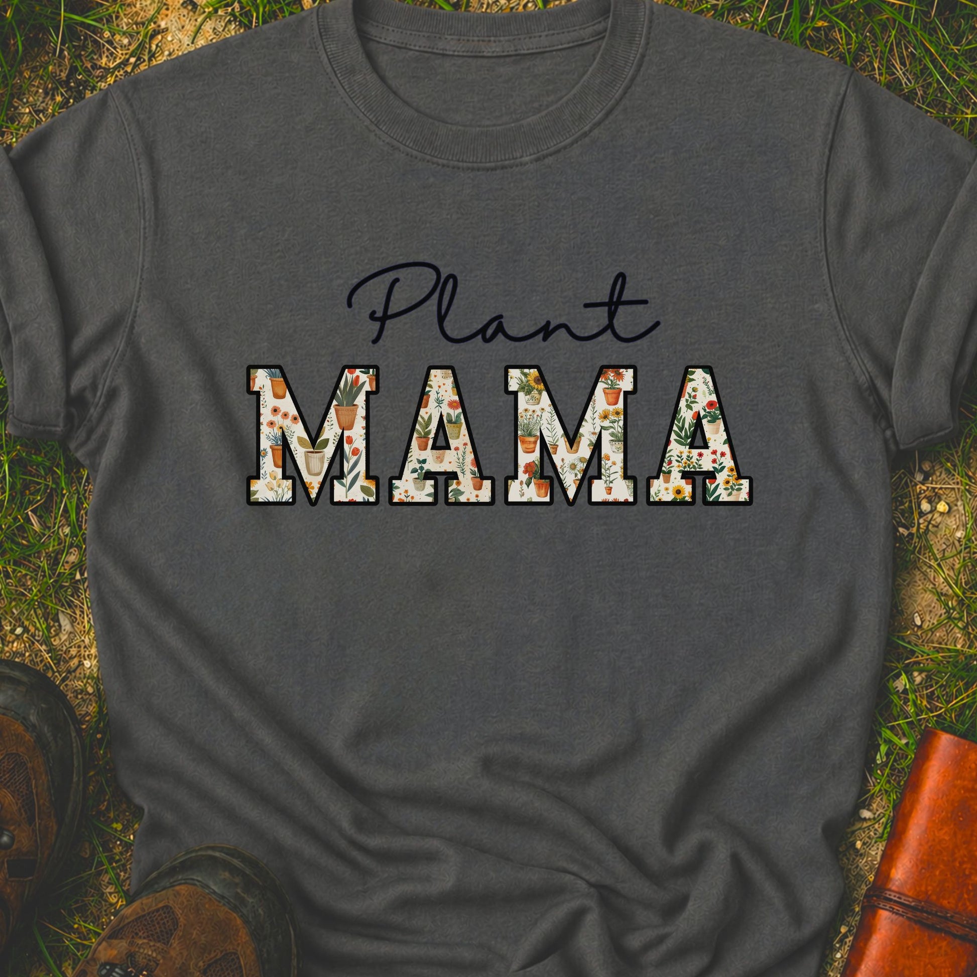 Gray t-shirt with 'Plant MAMA' text filled with cheerful potted plants and florals within the letters.  The tee is lying flat on grass