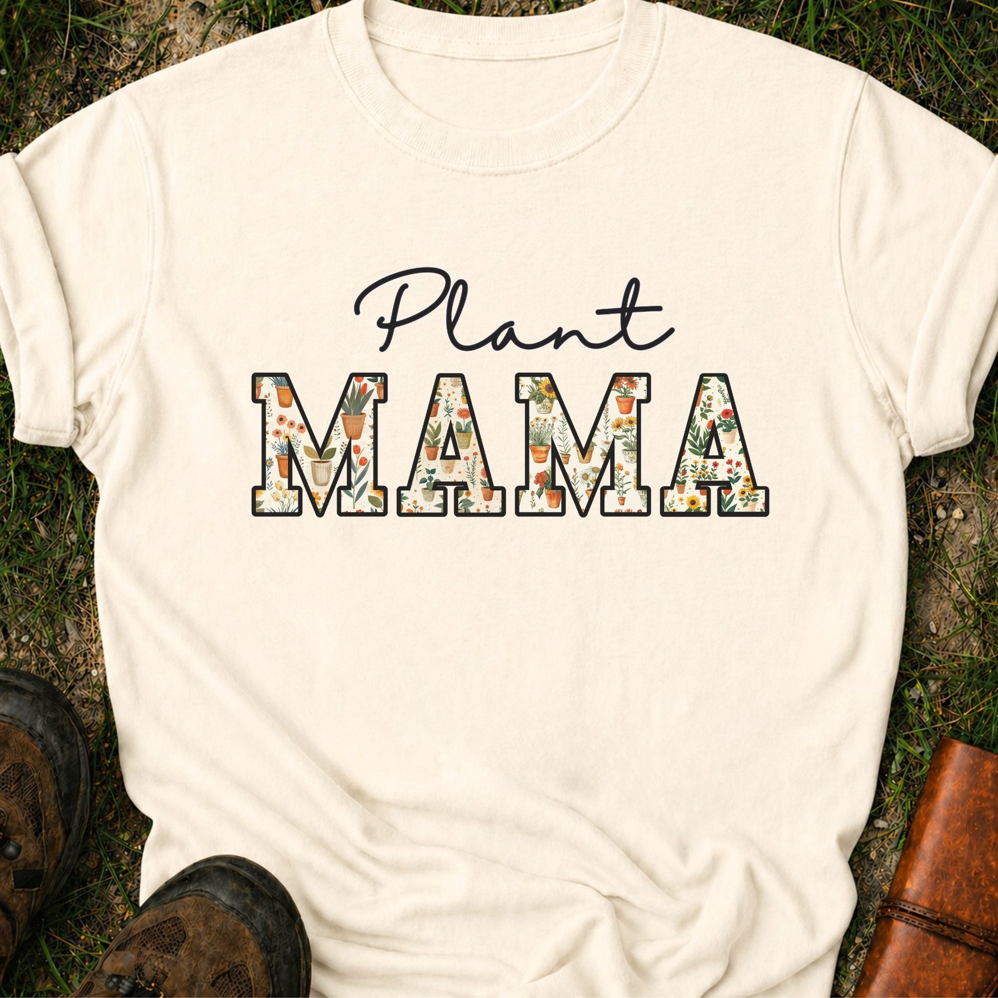 Ivory t-shirt with 'Plant MAMA' text filled with cheerful potted plants and florals within the letters.  The tee is lying flat on grass