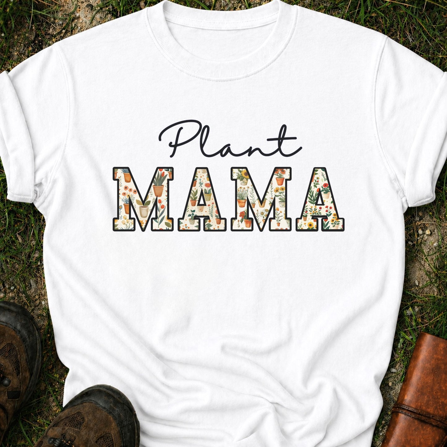 Whitet-shirt with 'Plant MAMA' text filled with cheerful potted plants and florals within the letters.  The tee is lying flat on grass