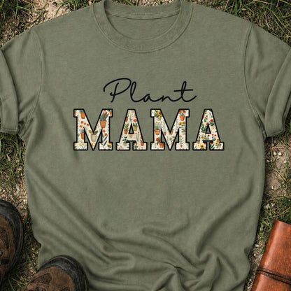 Green t-shirt with 'Plant MAMA' text filled with cheerful potted plants and florals within the letters.  The tee is lying flat on grass