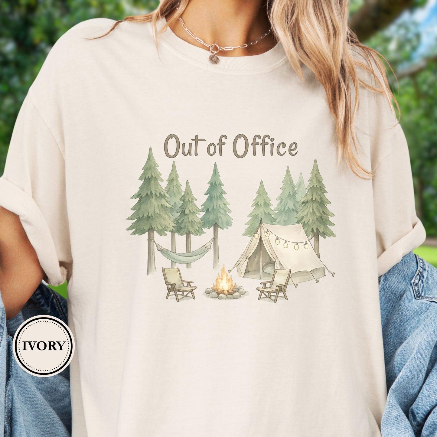 Model is wearing an Ivory t-shirt with camping graphic featuring pine trees, a tent, hammock, campfire, and the phrase “Out of Office.”
