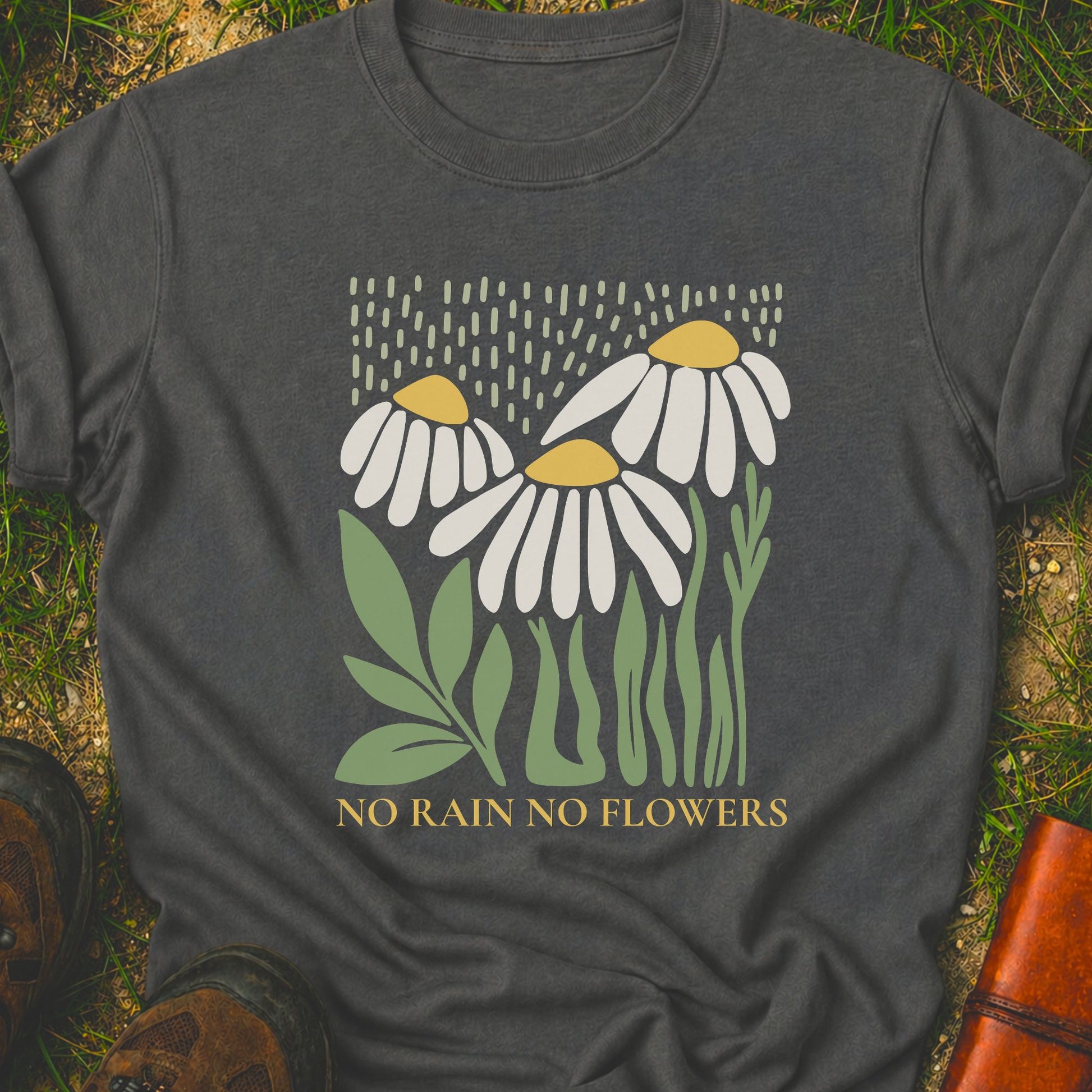 Dark Grey T-Shirt with 3 boho style flowers in the rain with the text "No Rain No Flowers".  Tshirt is lying flat on grass.