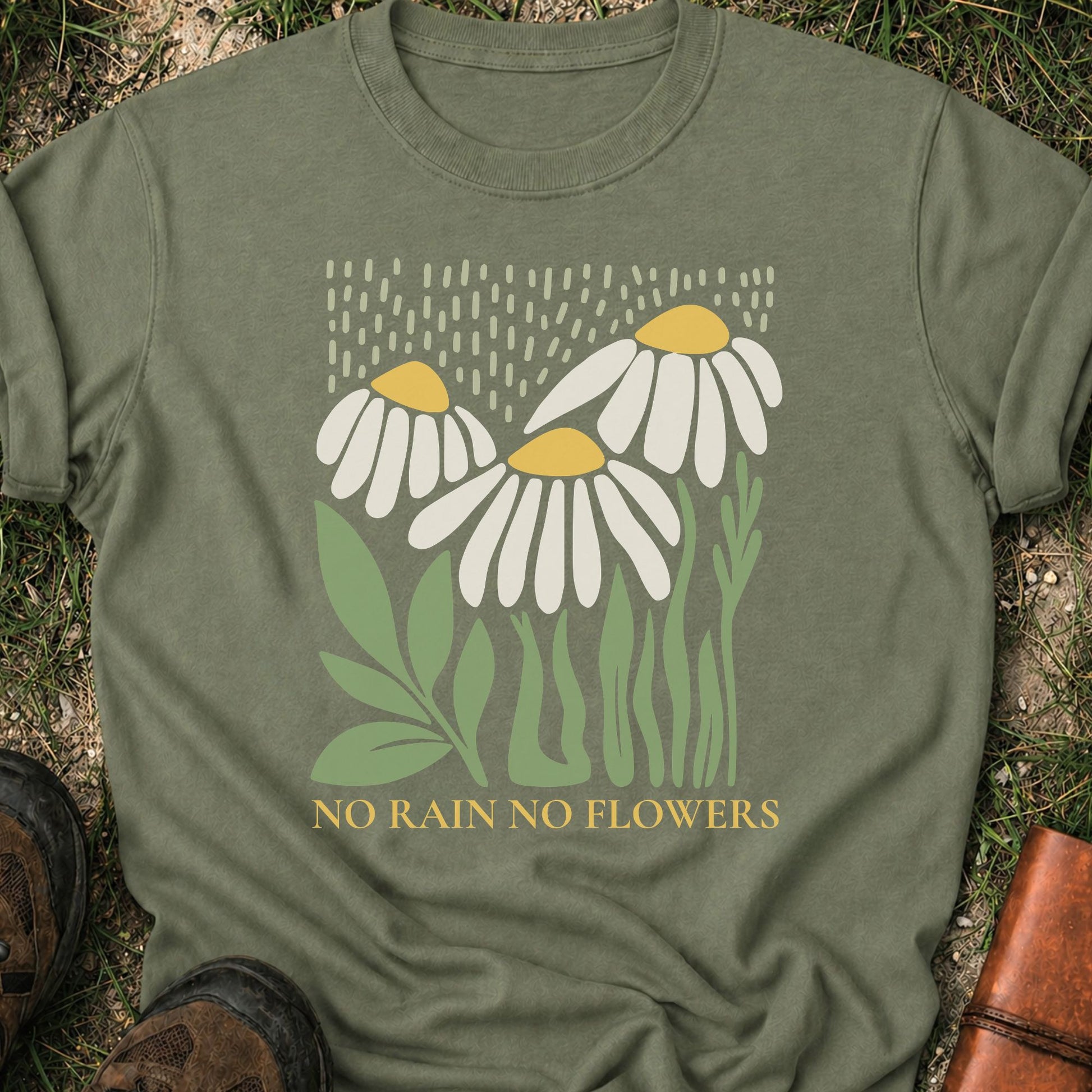 Moss Green T-Shirt with 3 boho style flowers in the rain with the text "No Rain No Flowers".  Tshirt is lying flat on grass.