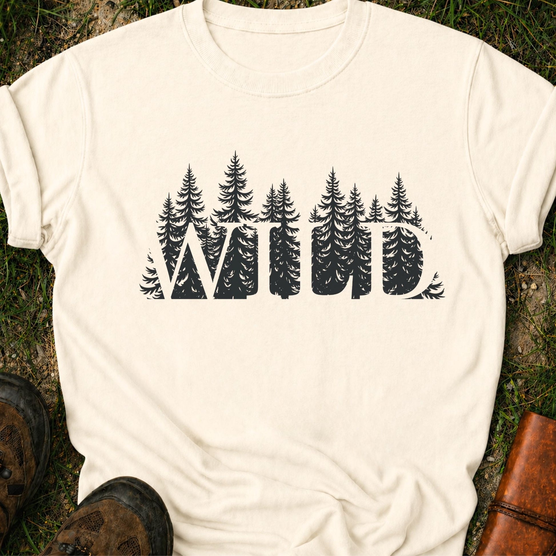Ivory t-shirt with the word WILD cut into a  forest design lying on grass