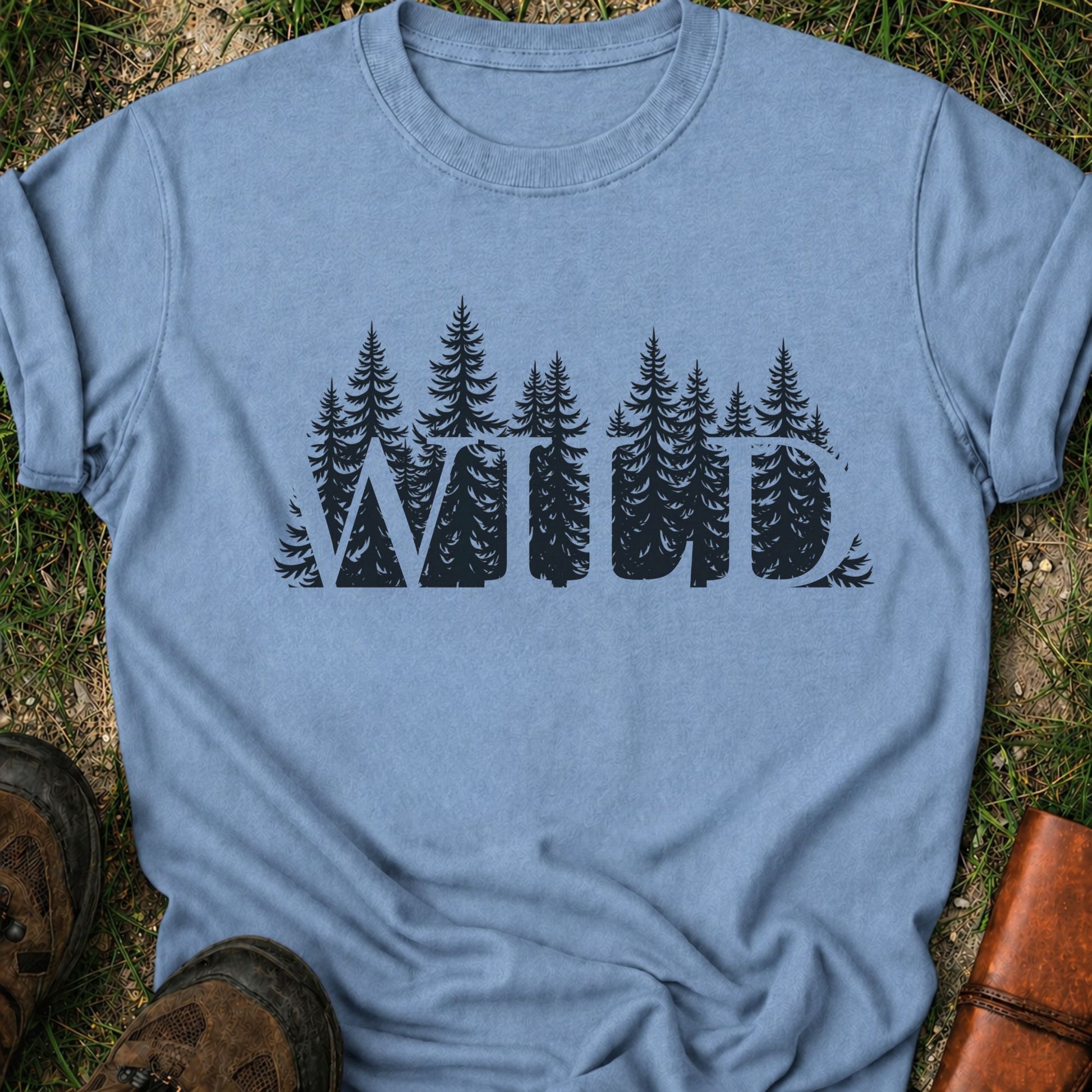 Light Blue t-shirt with the word WILD cut into a  forest design lying on grass