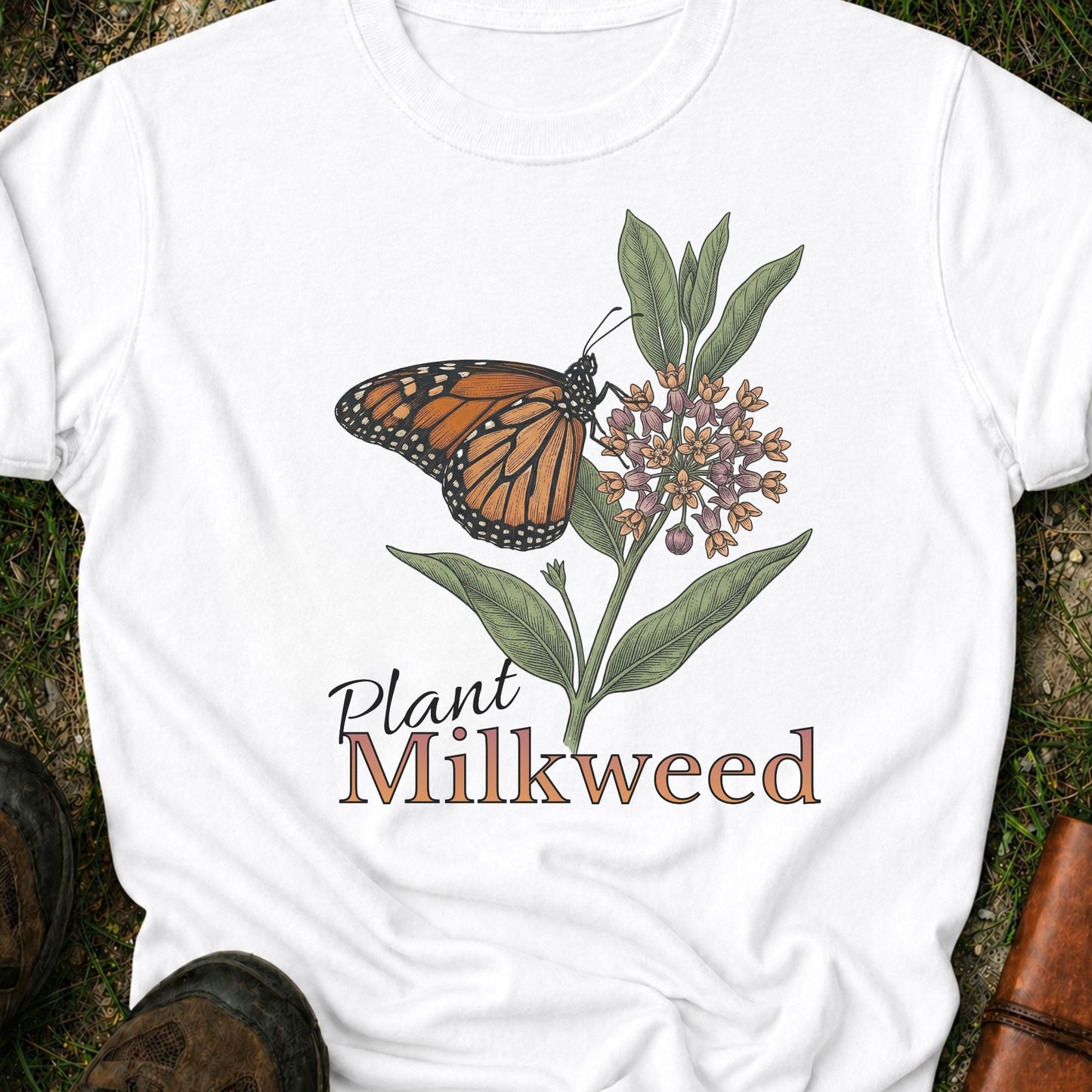 White t-shirt with a butterfly and milkweed design  and the caption Plant Milkweed lying  on the grass