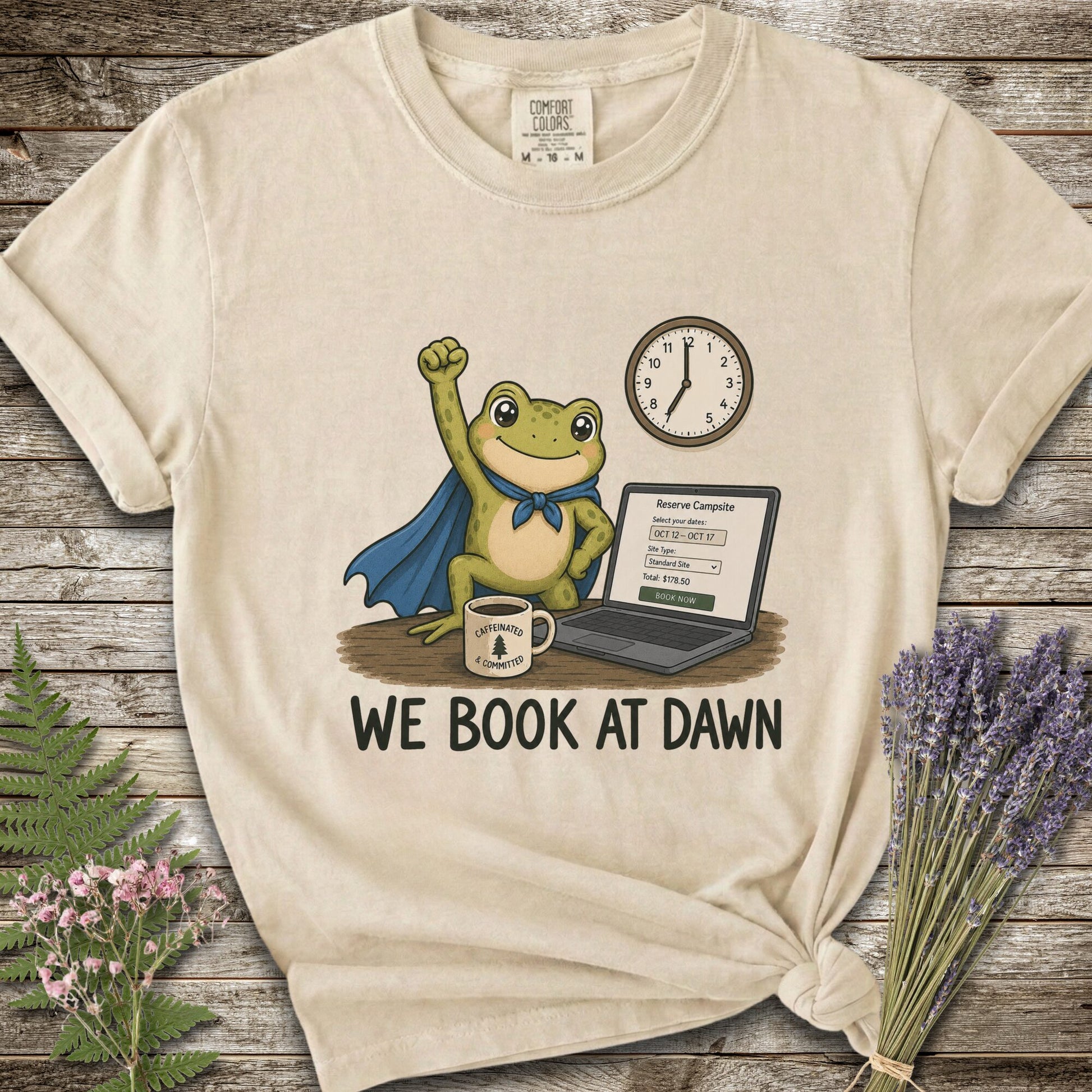 Ivory T-shirt with the image of a frod with his fist raised in front of a computer with the phrase "We Book At Dawn"