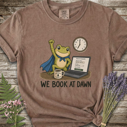 Brown T-shirt with the image of a frod with his fist raised in front of a computer with the phrase "We Book At Dawn"