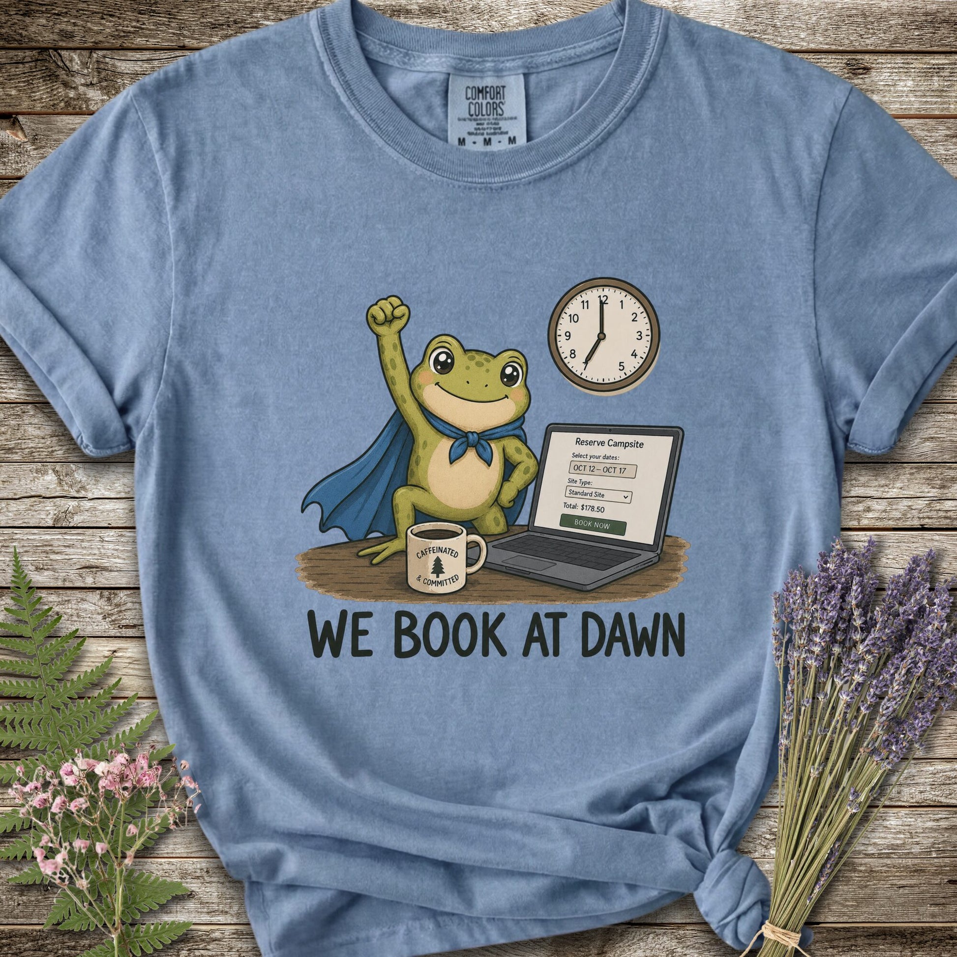 Blue T-shirt with the image of a frod with his fist raised in front of a computer with the phrase "We Book At Dawn"