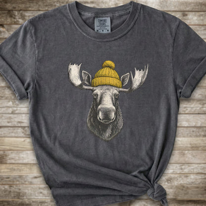 A dark grey short-sleeve t-shirt with a graphic of a moose wearing a yellow knit beanie, displayed on a rustic wooden background.