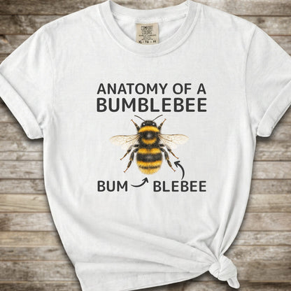 A  white graphic t-shirt with a knot at the bottom right, featuring a bumblebee illustration and the text 'ANATOMY OF A BUMBLEBEE' and 'BUM  BLEBEE'. The shirt is displayed flat on a rustic wooden background.