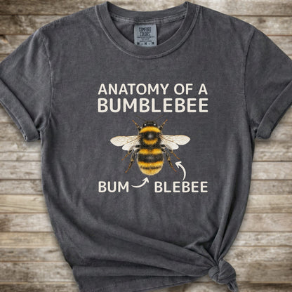 A dark grey graphic t-shirt with a knot at the bottom right, featuring a bumblebee illustration and the text 'ANATOMY OF A BUMBLEBEE' and 'BUM  BLEBEE'. The shirt is displayed flat on a rustic wooden background.