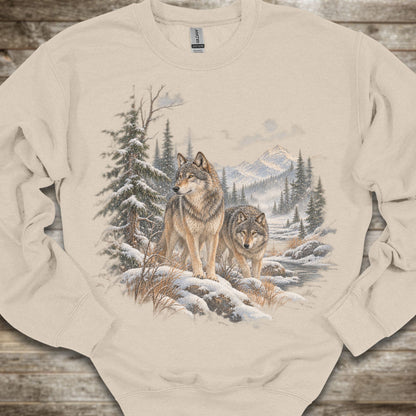 A beige crewneck sweatshirt featuring a detailed graphic print of two wolves in a snowy winter forest, laid flat on a rustic wooden background.