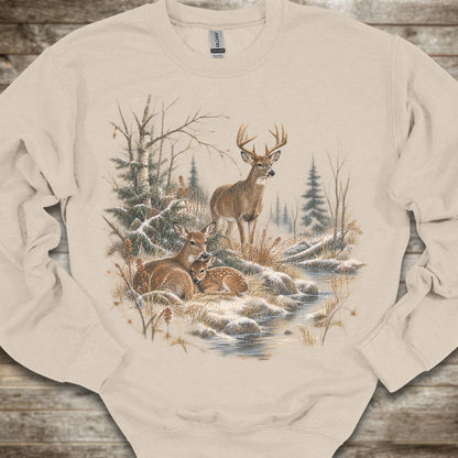 A beige crewneck sweatshirt featuring a detailed winter forest graphic with deer, trees, and a stream, laid flat on a rustic wooden background.