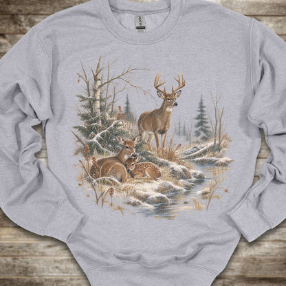 A light gray crewneck sweatshirt featuring a detailed graphic print of a winter forest scene with deer, trees, and a stream, laid flat on a rustic wooden surface.