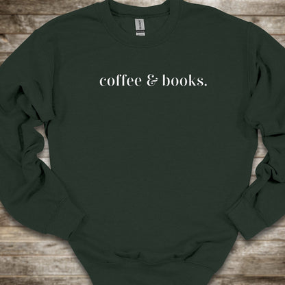 A dark forest green crewneck sweatshirt with the phrase 'coffee & books.' printed in white serif text across the chest, laid flat on a rustic wooden background.