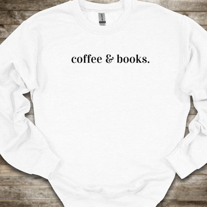 A white crewneck sweatshirt with the phrase 'coffee & books.' printed in black serif font across the chest, laid flat on a rustic wooden background.