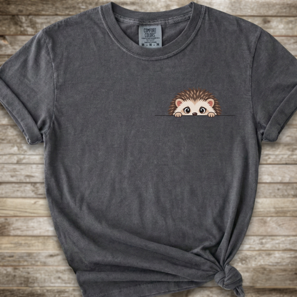 A dark gray  t-shirt with a cute cartoon hedgehog peeking out from the chest pocket, styled with a knot at the bottom hem against a rustic wooden background.