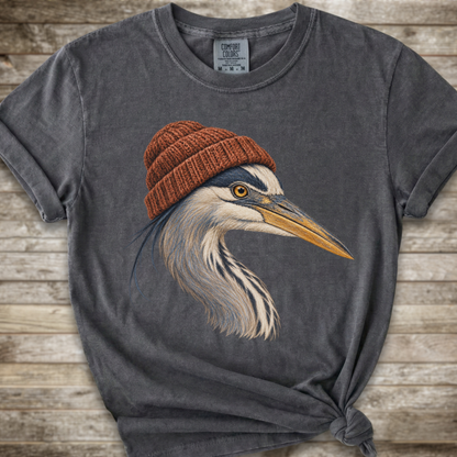 A dark gray t-shirt with a graphic of a heron wearing a brown knit beanie, laid flat on a rustic wooden background.