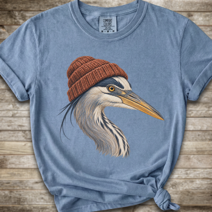 A light blue t-shirt with a graphic of a heron wearing a brown knit beanie, styled on a rustic wooden background.