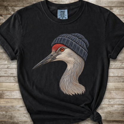 A black short-sleeve t-shirt with a graphic of a crane wearing a gray knit beanie, displayed on a rustic wooden background.