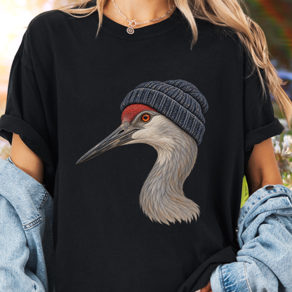 A person wearing a black oversized T-shirt with a large graphic of a crane wearing a gray knit beanie. The person has blonde hair, a silver necklace, and is wearing a light blue denim jacket draped off the shoulders.