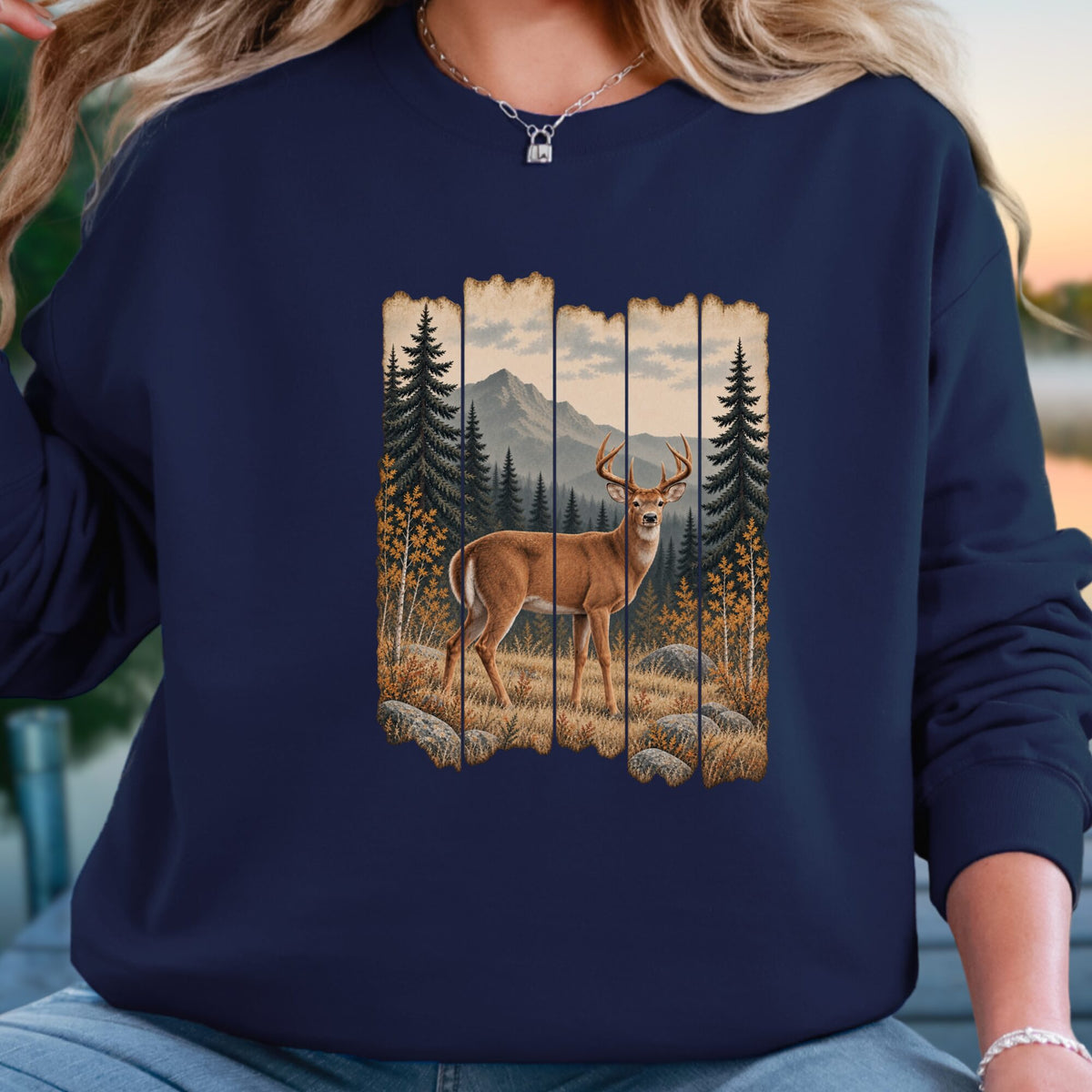 A woman wearing a navy blue sweatshirt with a vertical slat-style graphic print of a deer in a mountain pine forest, shown in a lifestyle setting.