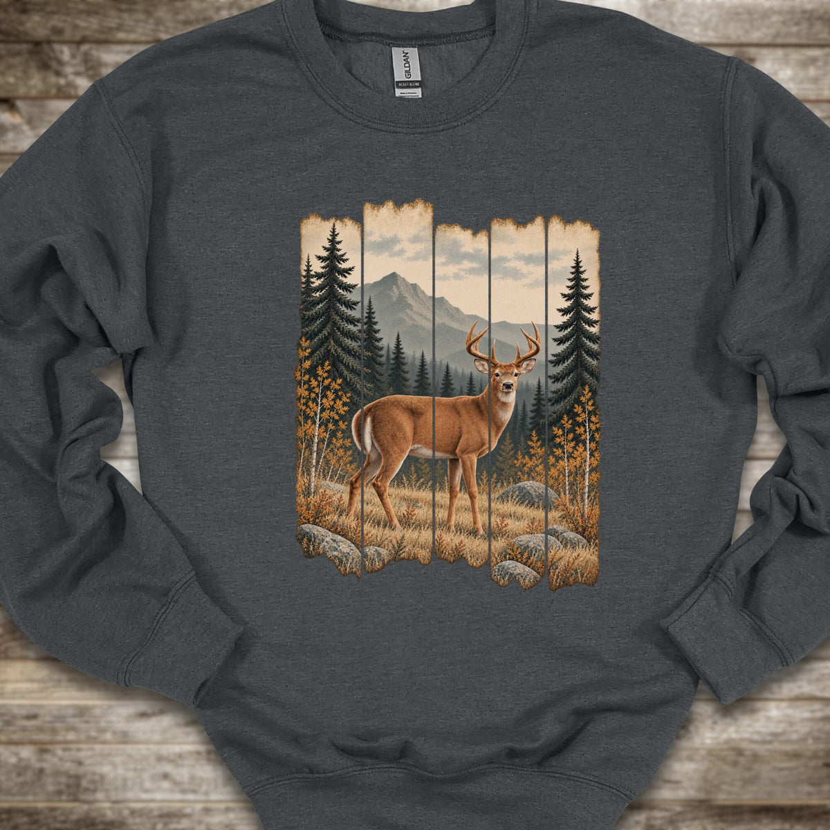A dark heather gray crewneck sweatshirt featuring a large graphic print of a deer in a forest with mountains in the background, laid flat on a rustic wood surface.