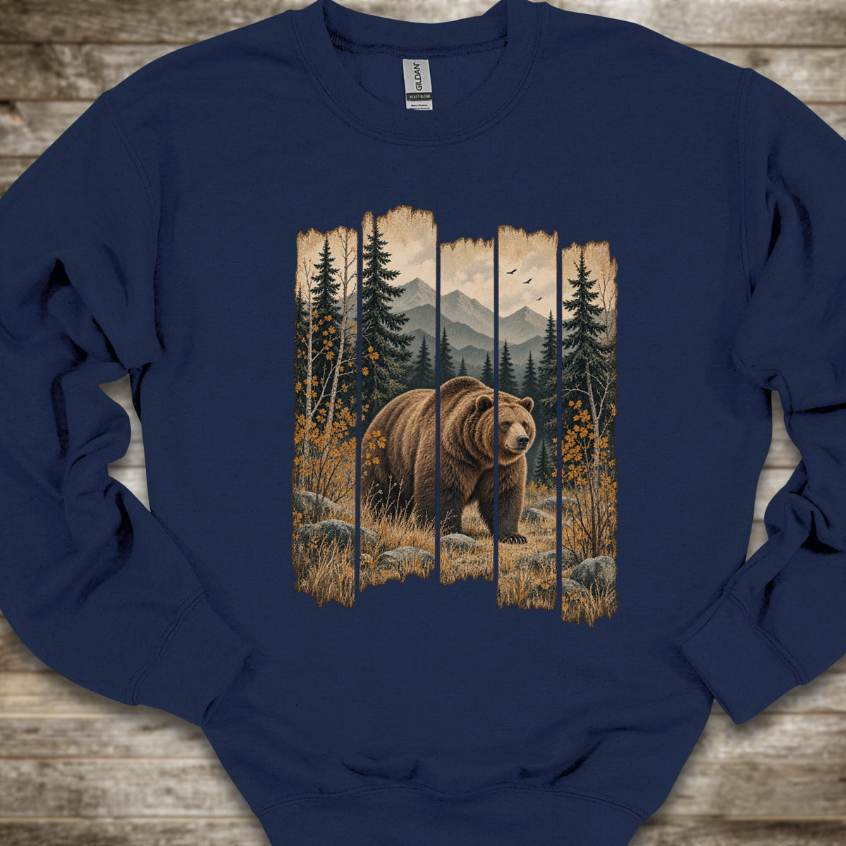 A navy blue crewneck sweatshirt laid flat on a rustic wooden surface, featuring a large graphic print of a brown bear in a forest with mountains in the background.