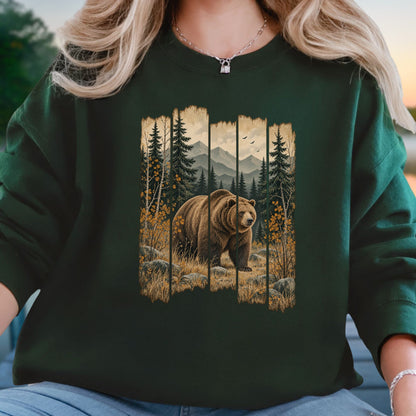 A person wearing a dark forest green crewneck sweatshirt with a large graphic print of a brown grizzly bear in a mountain pine forest. The person is also wearing blue jeans and a silver necklace.