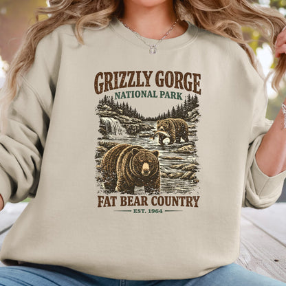 A woman wearing a beige crewneck sweatshirt with a rustic Grizzly Gorge National Park graphic featuring two bears and the text 'Fat Bear Country'.