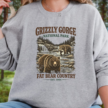 A person wearing a heather gray crewneck sweatshirt with a rustic brown and green Grizzly Gorge National Park graphic featuring bears, trees, and a waterfall.