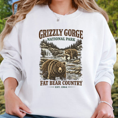 A woman wearing a white long-sleeve sweatshirt with a rustic Grizzly Gorge National Park graphic featuring brown bears and trees, with text reading 'Grizzly Gorge National Park' and 'Fat Bear Country Est. 1964'.