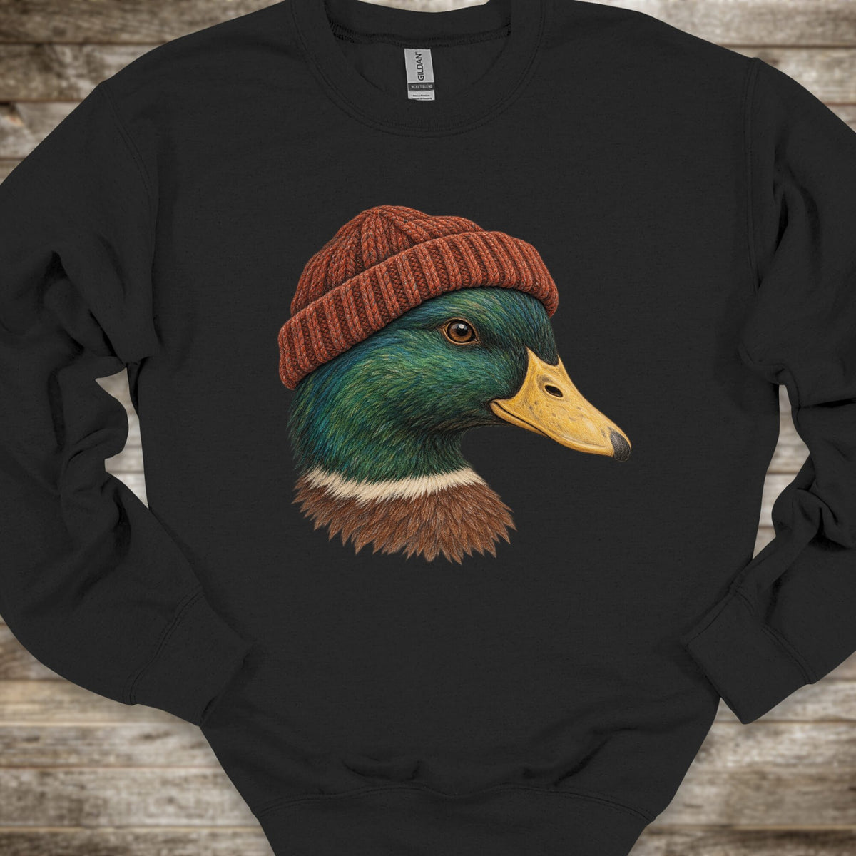 A black long-sleeve crewneck sweatshirt laid flat on a rustic wooden surface, featuring a graphic print of a mallard duck wearing a brown knit beanie.