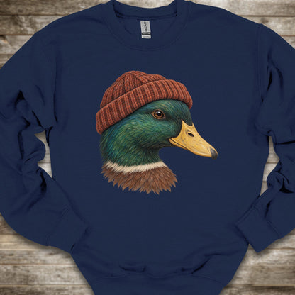 A navy blue crewneck sweatshirt featuring a graphic print of a mallard duck wearing a brown knit beanie, laid flat on a rustic wooden background.