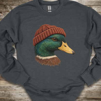 A dark gray crewneck sweatshirt featuring a graphic print of a mallard duck wearing a brown knit beanie, laid flat on a rustic wooden background.