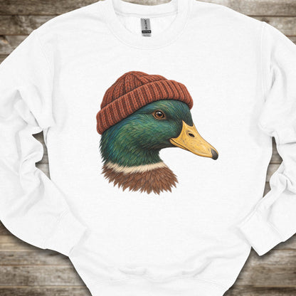 A white crewneck sweatshirt featuring a graphic print of a mallard duck wearing a brown knit beanie, laid flat on a rustic wooden background.