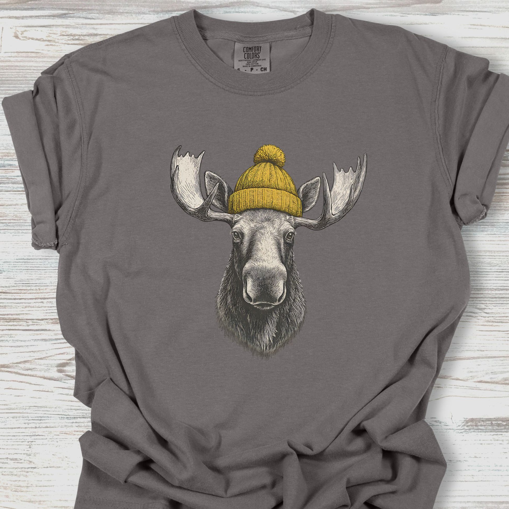 Gray t-shirt with a moose wearing a yellow beanie design on a wooden surface