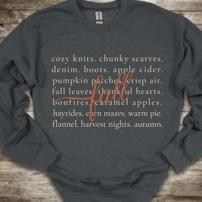 A dark charcoal gray crewneck sweatshirt with a cozy autumn-themed text graphic on the front, laid flat on a rustic wooden background.